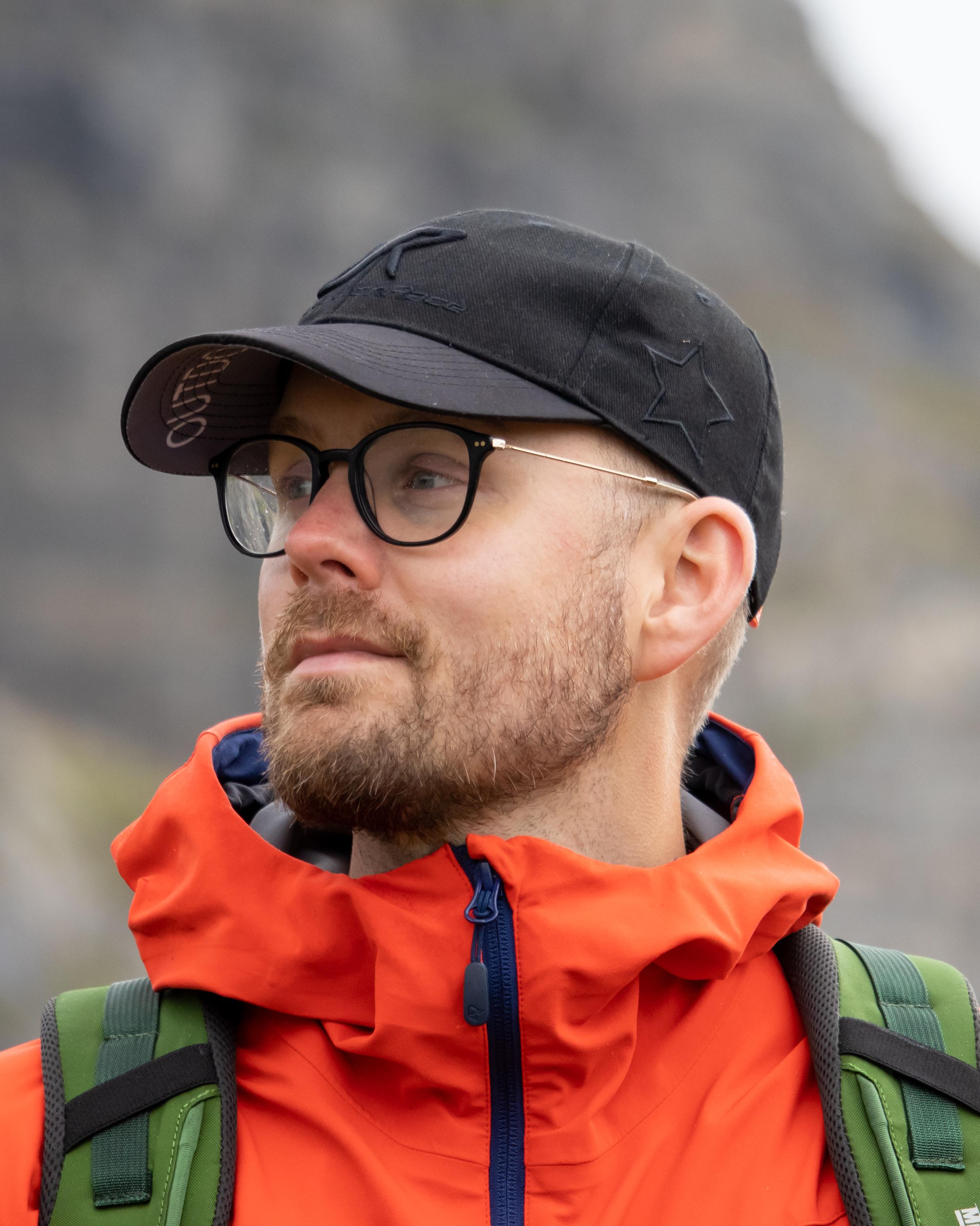 Jimmy Hultman i orange friluftsjacka, keps och glasögon ute i naturen.
